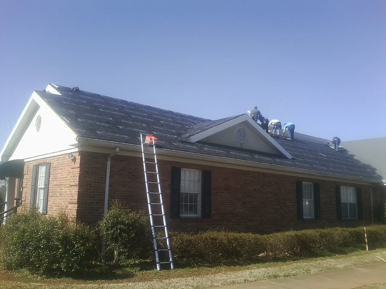 Crew tearing shingles off a brick ranch roof with a ladder set — Emergency Roof Repair work by our crew in Export