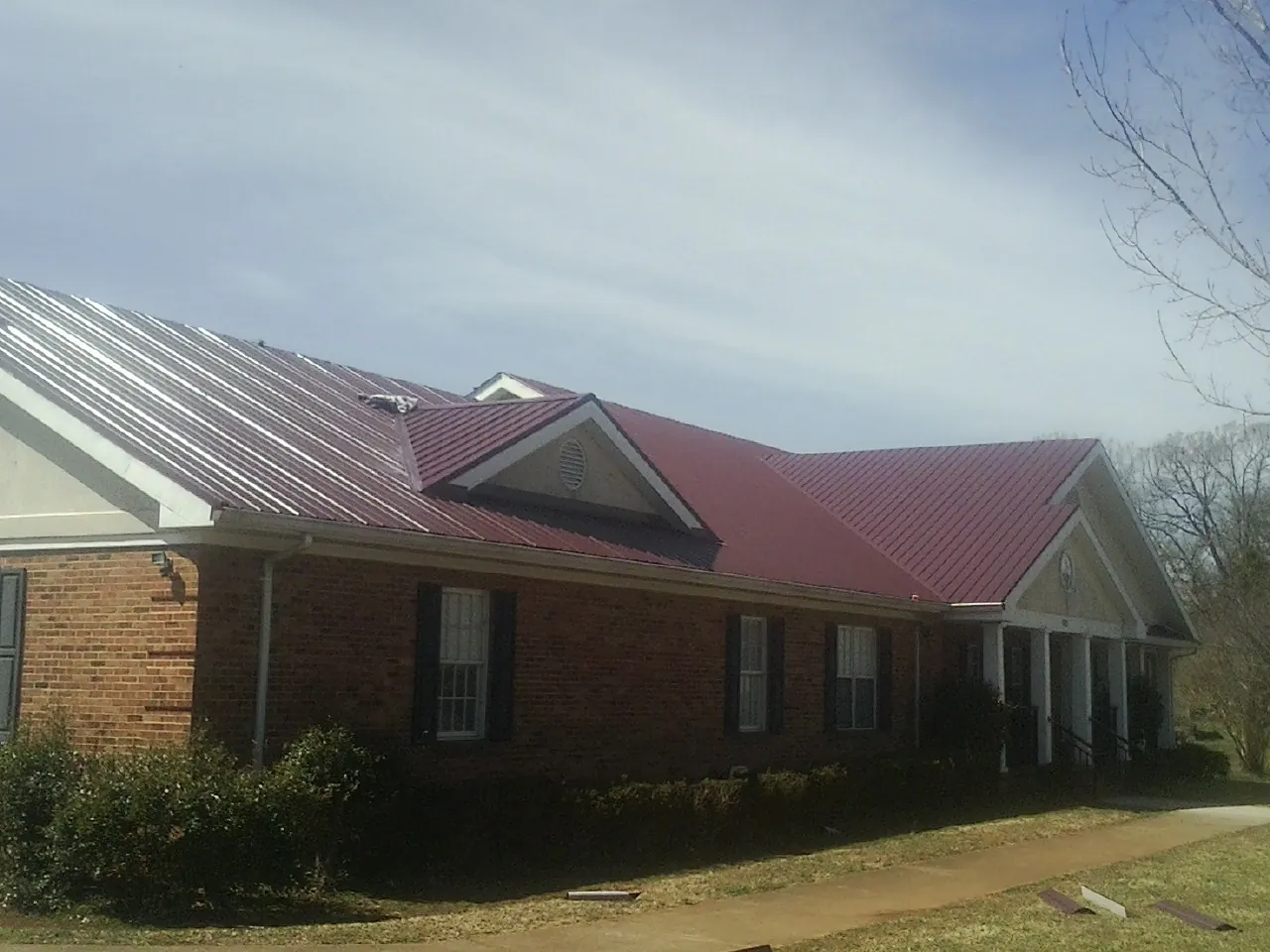 Red metal roof with gabled entries on a long brick building, from a Hail Damage Roof Repair job in Export
