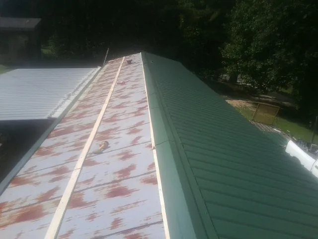 Old rusted panels beside newly installed green metal roofing — Wind Damage Roof Repair by Roofing Brothers in Export