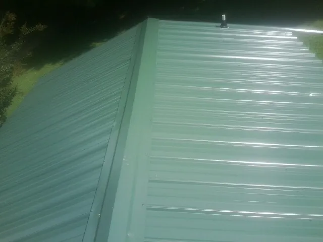 New green metal panels meeting at the ridge of a roof — Flat Roof Repair work by our crew in Export