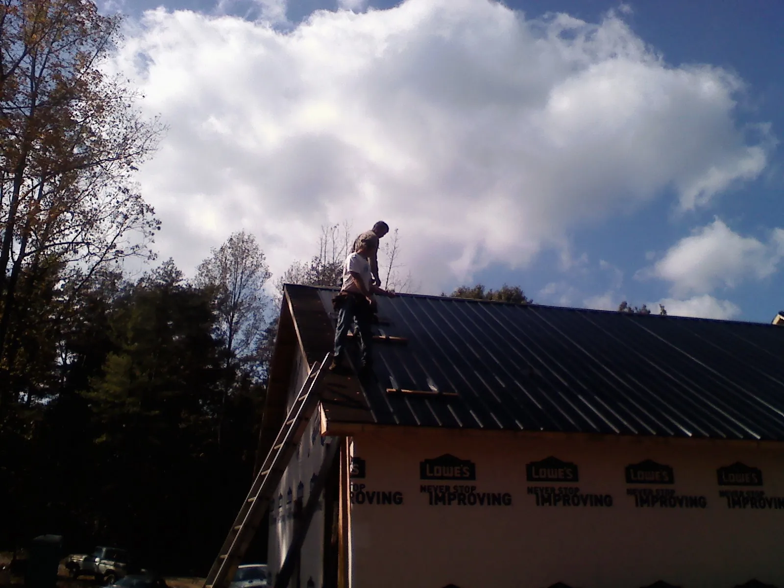 Roofer fastening dark metal panels high against a cloudy sky, from a Roof Inspection job in Export