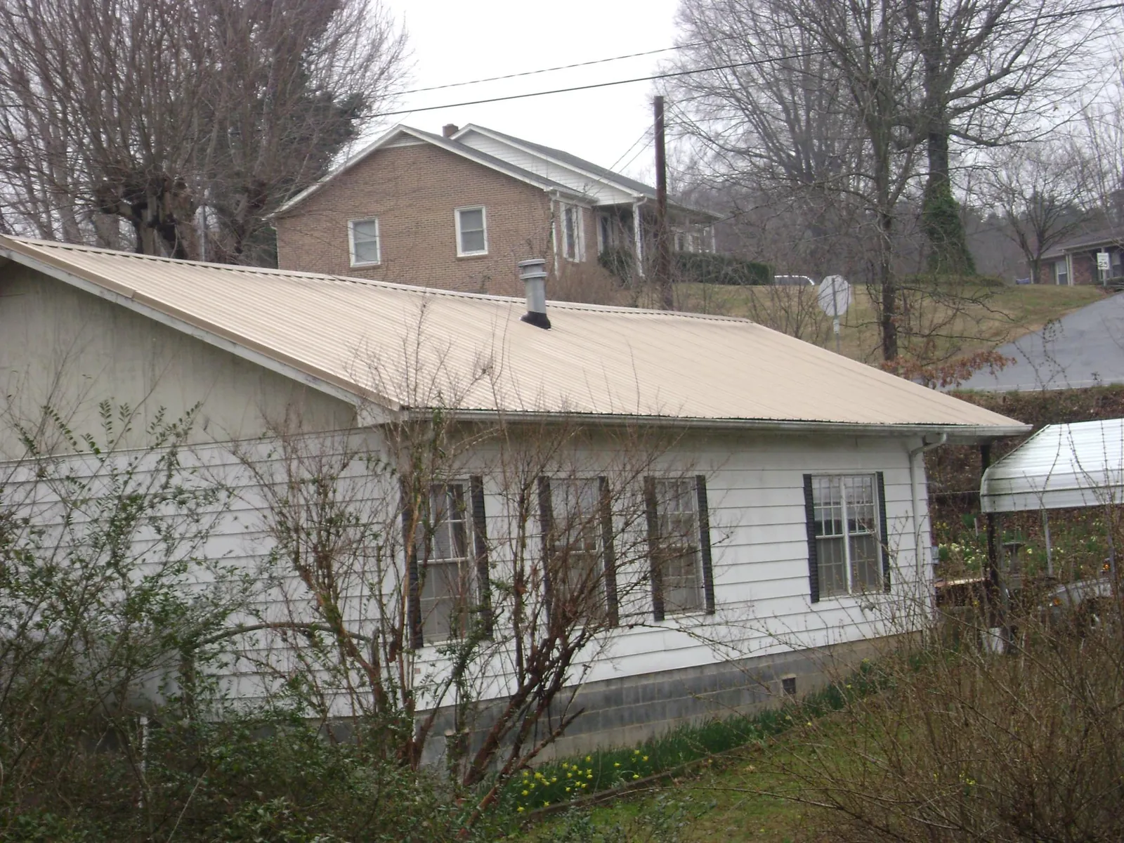 Tan metal roof on a white sided house set into a hillside — Commercial Roofing by Roofing Brothers in Export